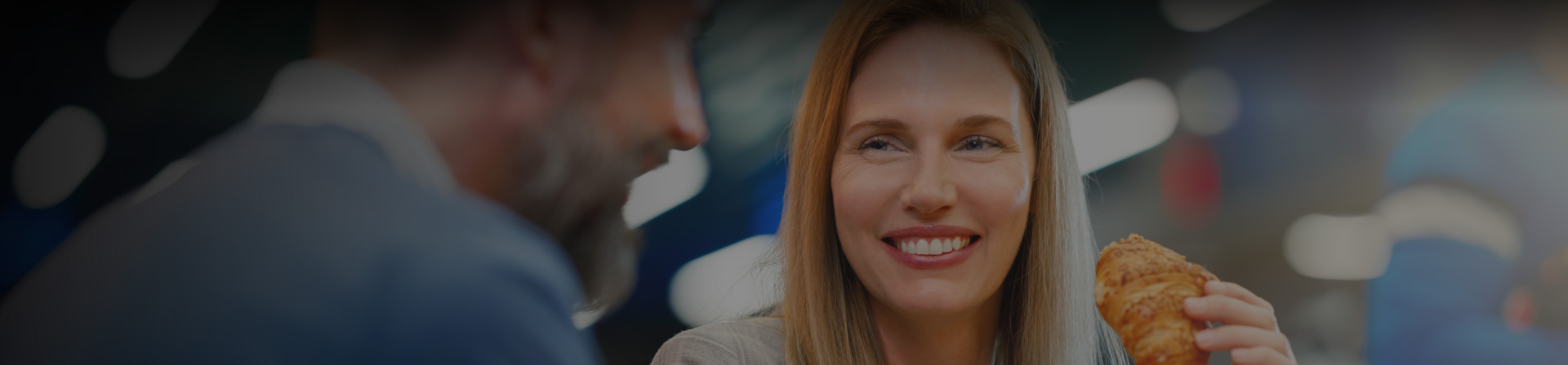 woman holding croissant smiling looking at a man